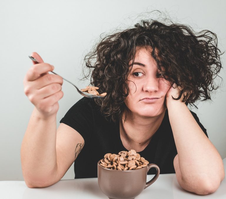 A woman looks unexcitedly at the cereal on her spoon. She needs help with binge eating disorder